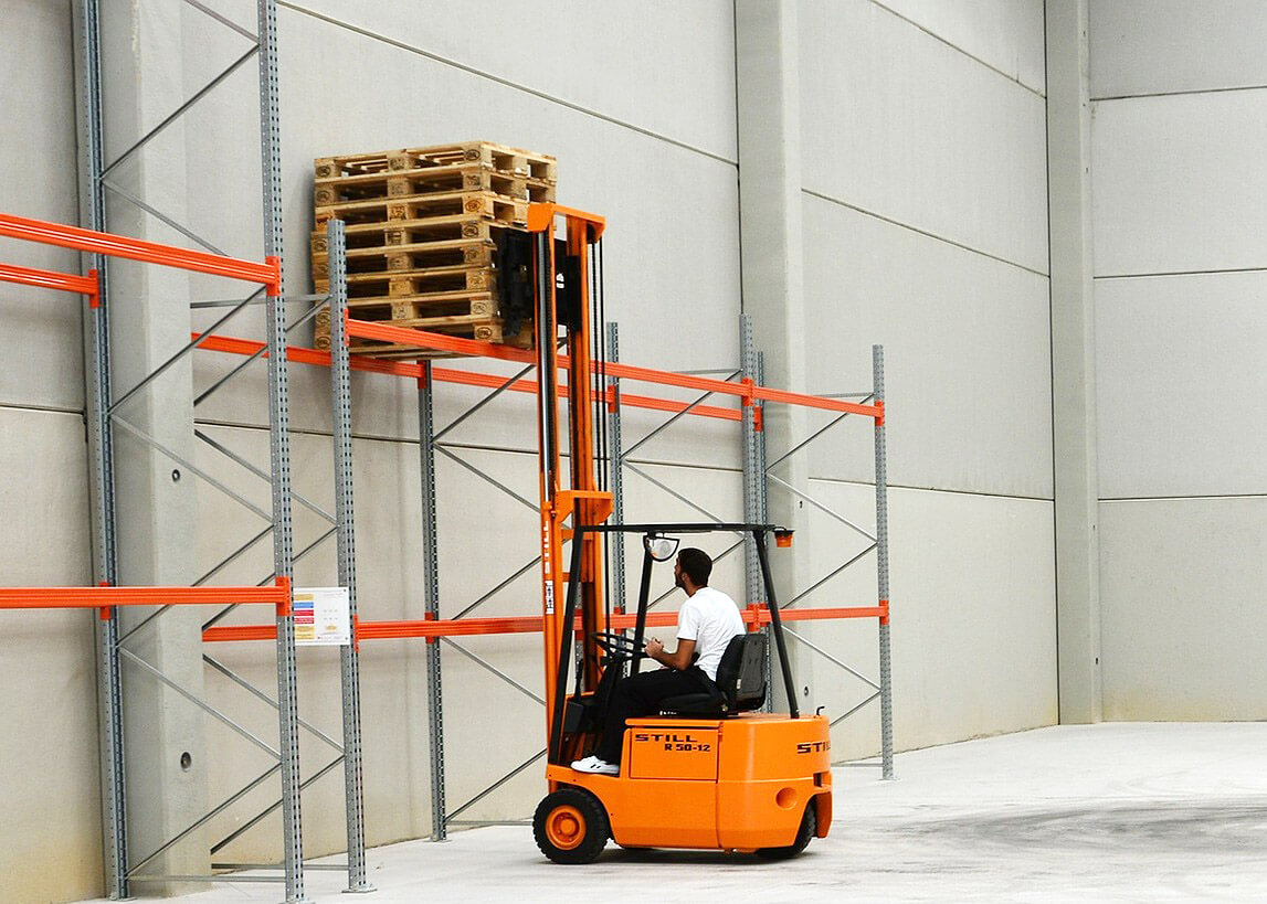 forklift operator shown placing stack of empty pallets on shelf